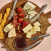 Wooden charcuterie board with assorted cheeses, meats, crackers, and strawberries on a pink background.