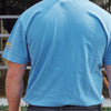 A person wearing a light blue Cabot x Always With Honor T-shirt by New Duds stands outdoors with their back to the camera near a metal fence, with part of an animal visible in the background.