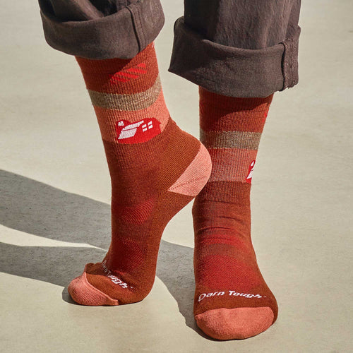 A person in brown pants and Cabot x Darn Tough Socks, Chestnut by Darn Tough Vermont, stands on a light surface—ideal for Vermont Adaptive adventures.