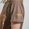 A person wearing the New Duds Cabot x Always With Honor T-shirt in Espresso, featuring a floral design on the front and yellow-green "CABOT X ALWAYS WITH HONOR" text on the sleeve.