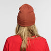A person with long blonde hair is seen from behind, wearing a red New Duds Life is Cheddar in Vermont Patch Beanie and a matching red shirt, set against a plain light gray background.