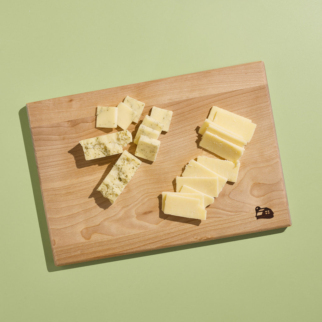 Cabot Cutting Board with cheese cut up on it on a green background