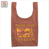 The Cabot x Always With Honor Baggu by Baggu is a reusable brown Vermont tote featuring pixel art of a farm, tractor, cow, and flowers with FRESH FROM VERMONT text. A corner label notes 10% of sales are donated. Proudly celebrates Green Mountain heritage.