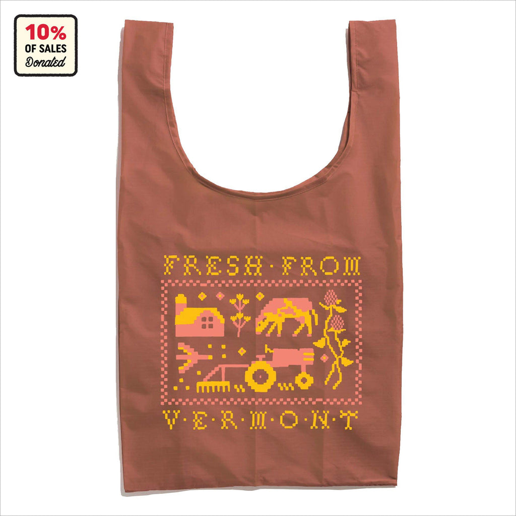 The Cabot x Always With Honor Baggu by Baggu is a reusable brown Vermont tote featuring pixel art of a farm, tractor, cow, and flowers with FRESH FROM VERMONT text. A corner label notes 10% of sales are donated. Proudly celebrates Green Mountain heritage.