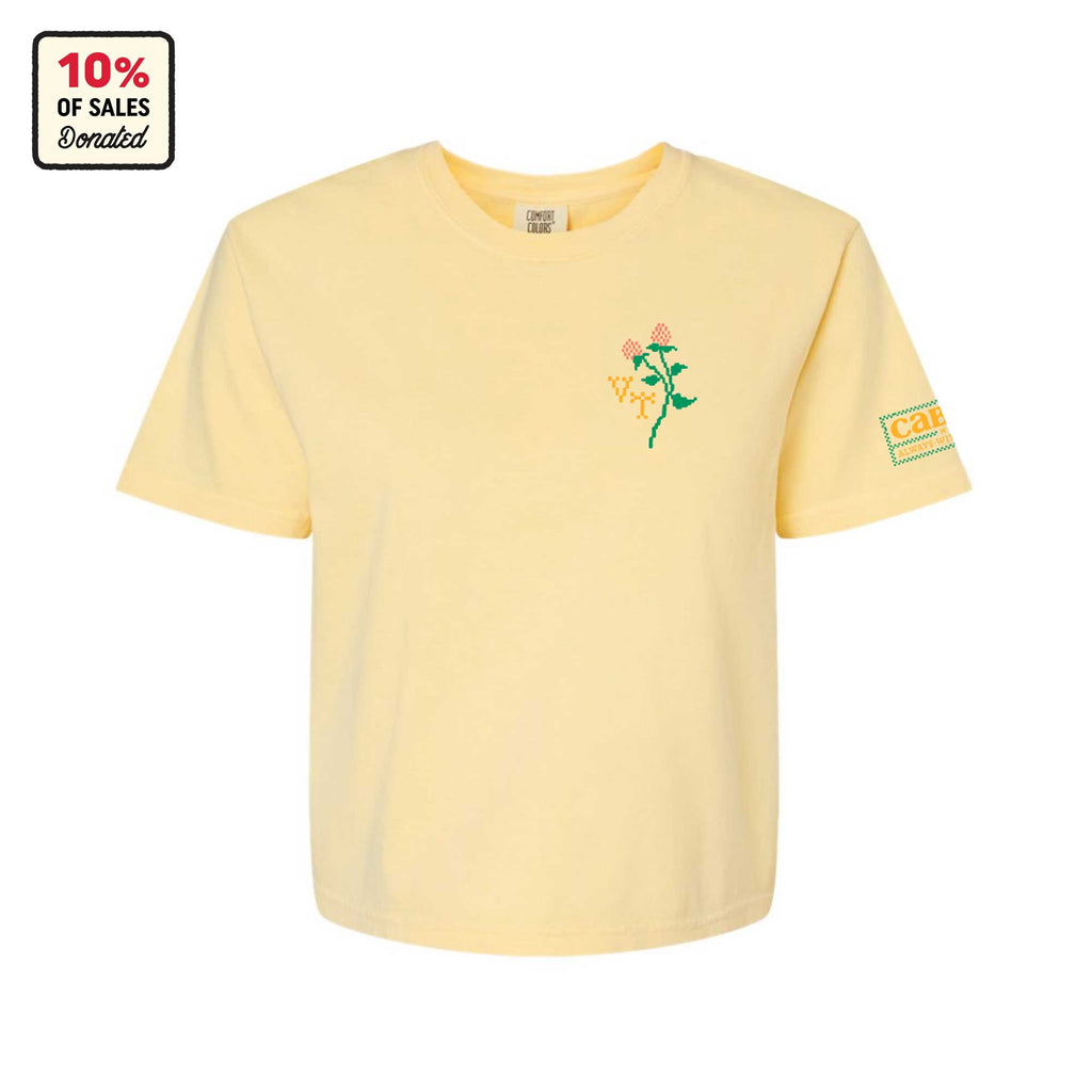 The Cabot x Always With Honor Crop T-shirt by New Duds is a light yellow heavyweight boxy tee featuring an embroidered flower and “Care” patch, with 10% of sales donated—perfect for Vermont-inspired style.