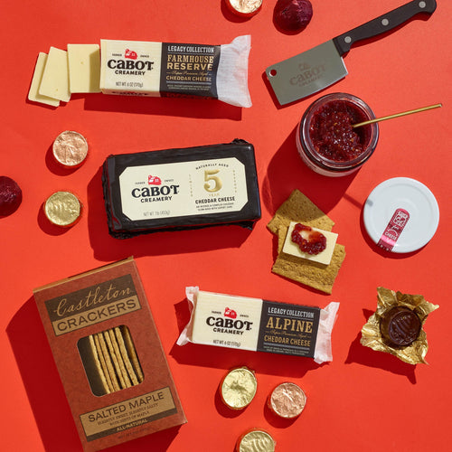 A flat lay of the Salty & Sweet Gift Pack by Cabot Creamery, featuring Vermont cheeses, salted maple Castleton crackers, jam with spreader, chocolate coins, and a mini cleaver—perfect for cheese and chocolate pairing.
