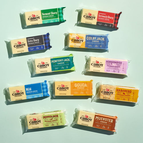 Twelve varieties of Cabot Creamery cheese blocks, including Vermont Sharp Cheddar, are arranged in colorful packaging—making the Cheese Block Party Pack a perfect gift for any cheese lover.