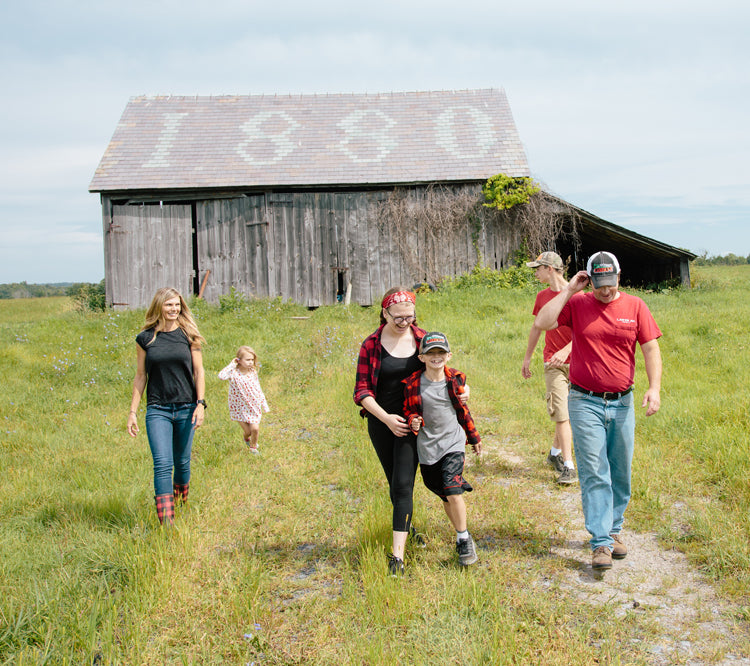 Cabot farm family walking through green field with barn in the background in vermont