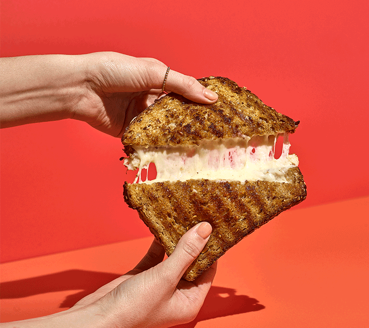 cheesy grilled cheese being pulled open on a two tone red background