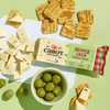 Cabot Creamery Pepper Jack Cheese, sliced into cubes and triangles, is arranged on a white board alongside green grapes and an assortment of crackers, all displayed on a light green surface.