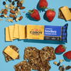 Sliced Cabot Creamery Extra Sharp Yellow Cheddar Cheese, multigrain crackers with seeds, strawberries, and mixed nuts on a blue background.