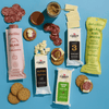 A selection from Cabot Creamery’s The Grazing Gift Box—including assorted cheese blocks, premium cheeses, cheese slices, salami, round crackers, honey, and mustard—is artfully arranged on a blue background with small stacks of cheese and artisan meats placed atop crackers.