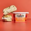 A tub of Cabot Creamery Garden Vegetable Cream Cheese next to two halves of a bagel sandwich filled with the savory spread.
