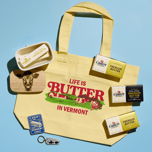 The Cabot Creamery Butter Lover’s Gift Box features a yellow tote bag with “Life is Butter in Vermont” printed on it, surrounded by Cabot butter packages, a cow-adorned butter dish, a Vermont patch, and a checkered keychain—making it the perfect gift or addition for any true butter enthusiast.