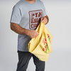 A person wearing a light gray T-shirt and dark pants holds a yellow New Duds Life is Butter Tote, appearing to open or organize it. The upper part of their face is not visible, lending a touch of Vermont charm.