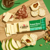 A wooden board featuring Cabot Creamery Vermont Sharp Cheddar Cheese, cheese slices, crackers, salami, pear slices, nuts, and fig jam is arranged neatly on a green background.