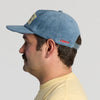 Man with a mustache wearing the New Duds Butter Corduroy Hat in blue and a yellow shirt, shown in left profile view against a plain light background.