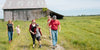 Cabot farm family walking through green field with barn in the background in vermont