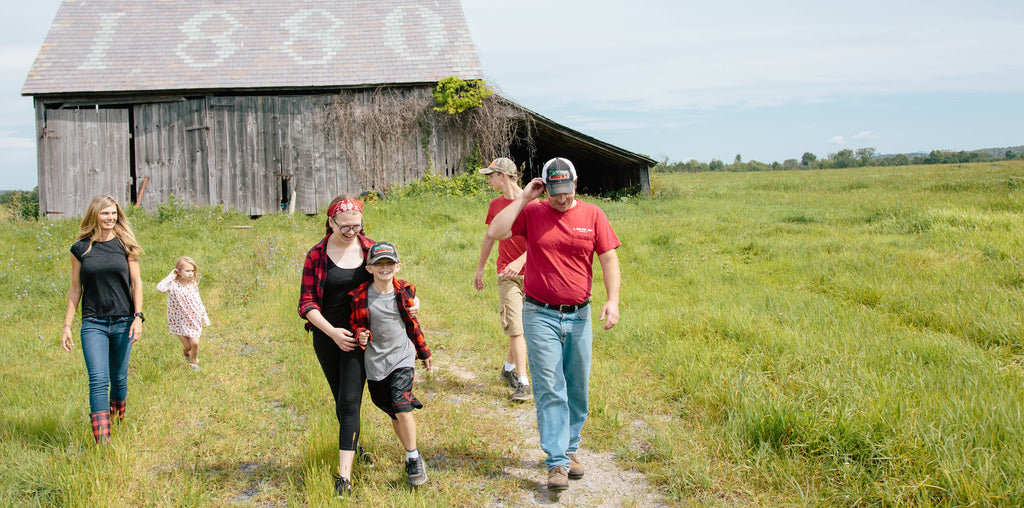Cabot farm family walking through green field with barn in the background in vermont