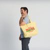 A smiling man with a mustache holds a Life is Butter Tote by New Duds, its bold red text and green accents celebrating Vermont’s dairy heritage and the Cabot cooperative, as he stands against a plain light background.