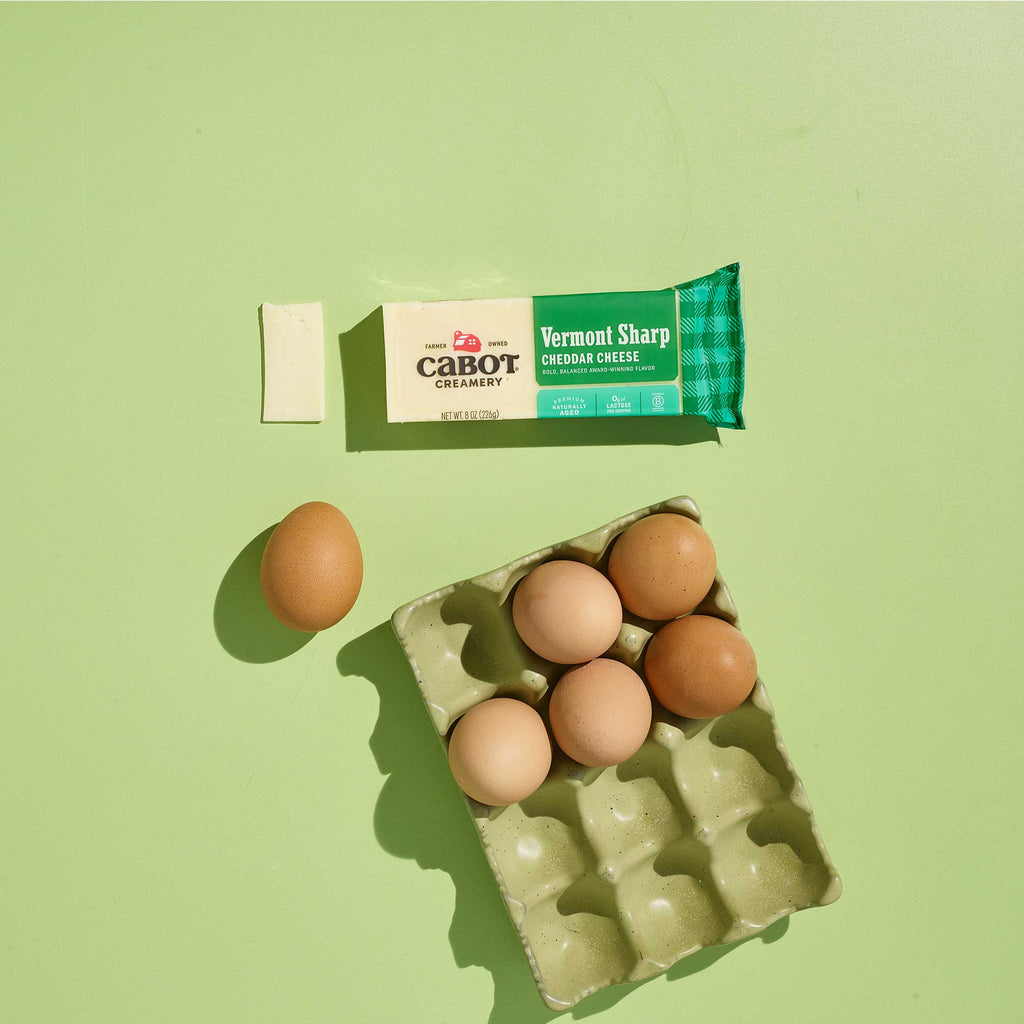 Carton of eggs with a block of Cabot Vermont Sharp Cheddar Cheese on a green background