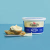 A container of Cabot Creamery Whipped Salted butter is placed beside two buttered bread slices and a knife, all on a blue surface with a blue background.