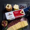 A slate board features slices of Cabot Creamerys Seriously Sharp Cheddar Cheese, elegantly arranged with crackers, salami, rosemary, grapes, and cranberries for a sophisticated display on a dark surface.